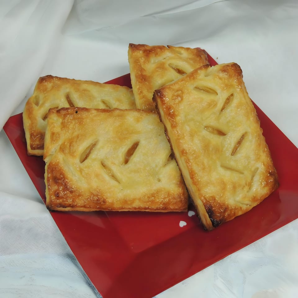 Four golden-brown apple turnovers with flaky crusts, arranged on a vibrant red plate.