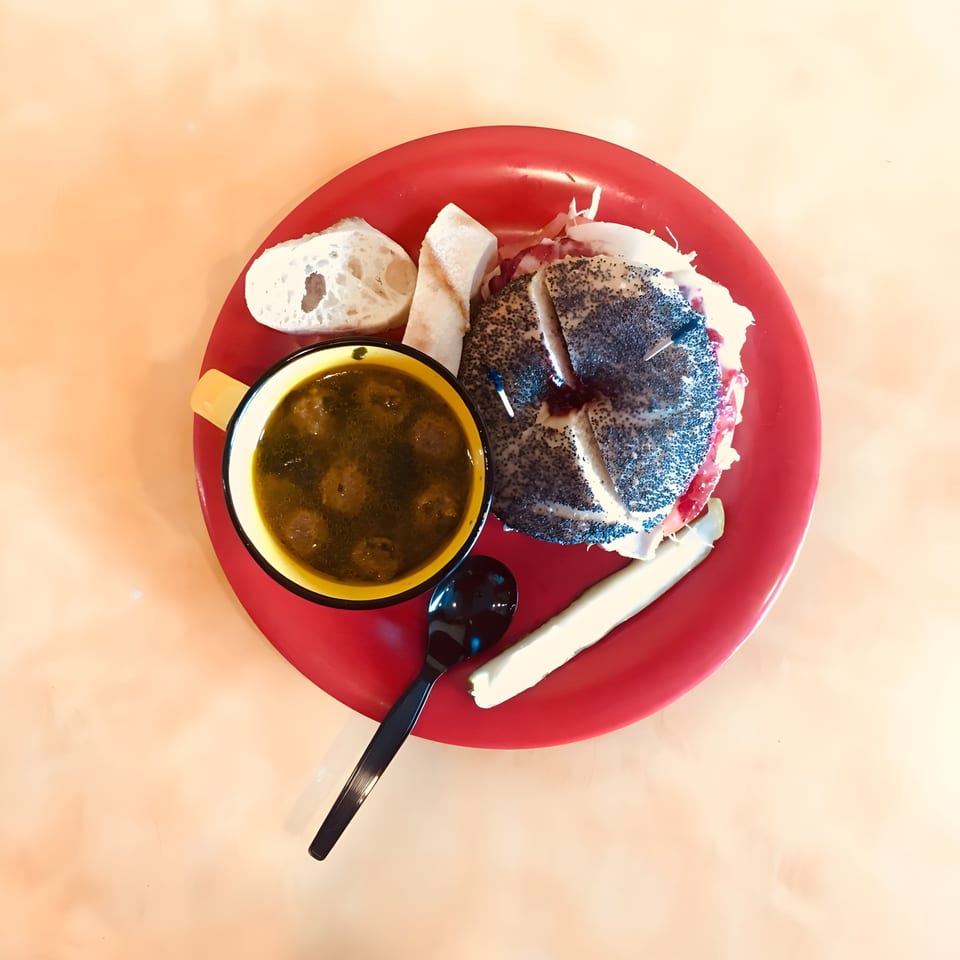 Ruby K's poppy seed bagel sandwich, soup, and bread on a red plate.