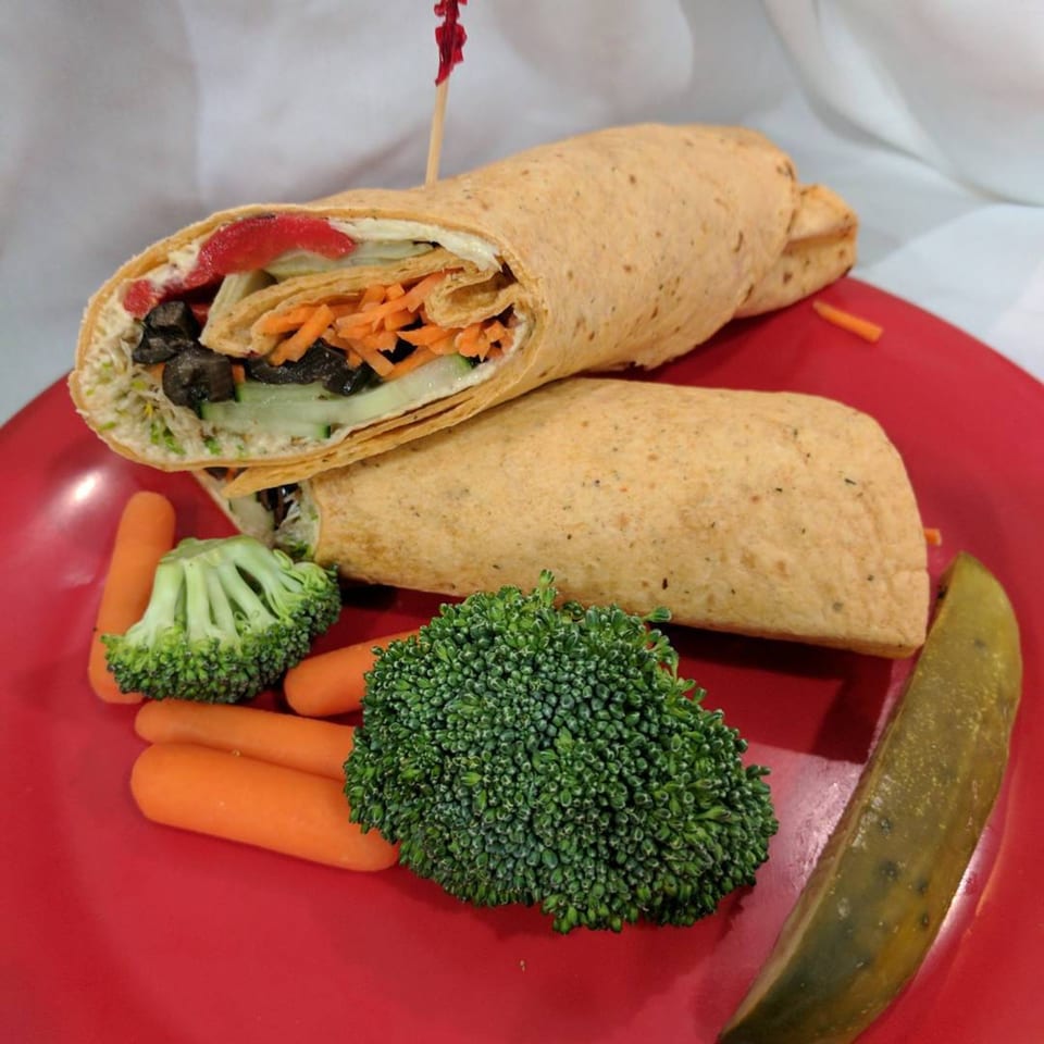 Two vegetable wraps with baby carrots, broccoli florets, and a pickle spear on a red plate.