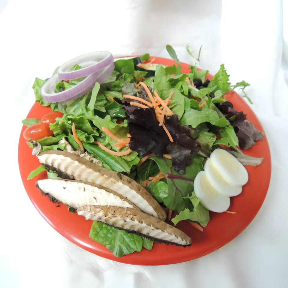 A vibrant Ruby K's Bagel Cafe salad with mixed greens, sliced mushrooms, hard-boiled eggs, and red onion.